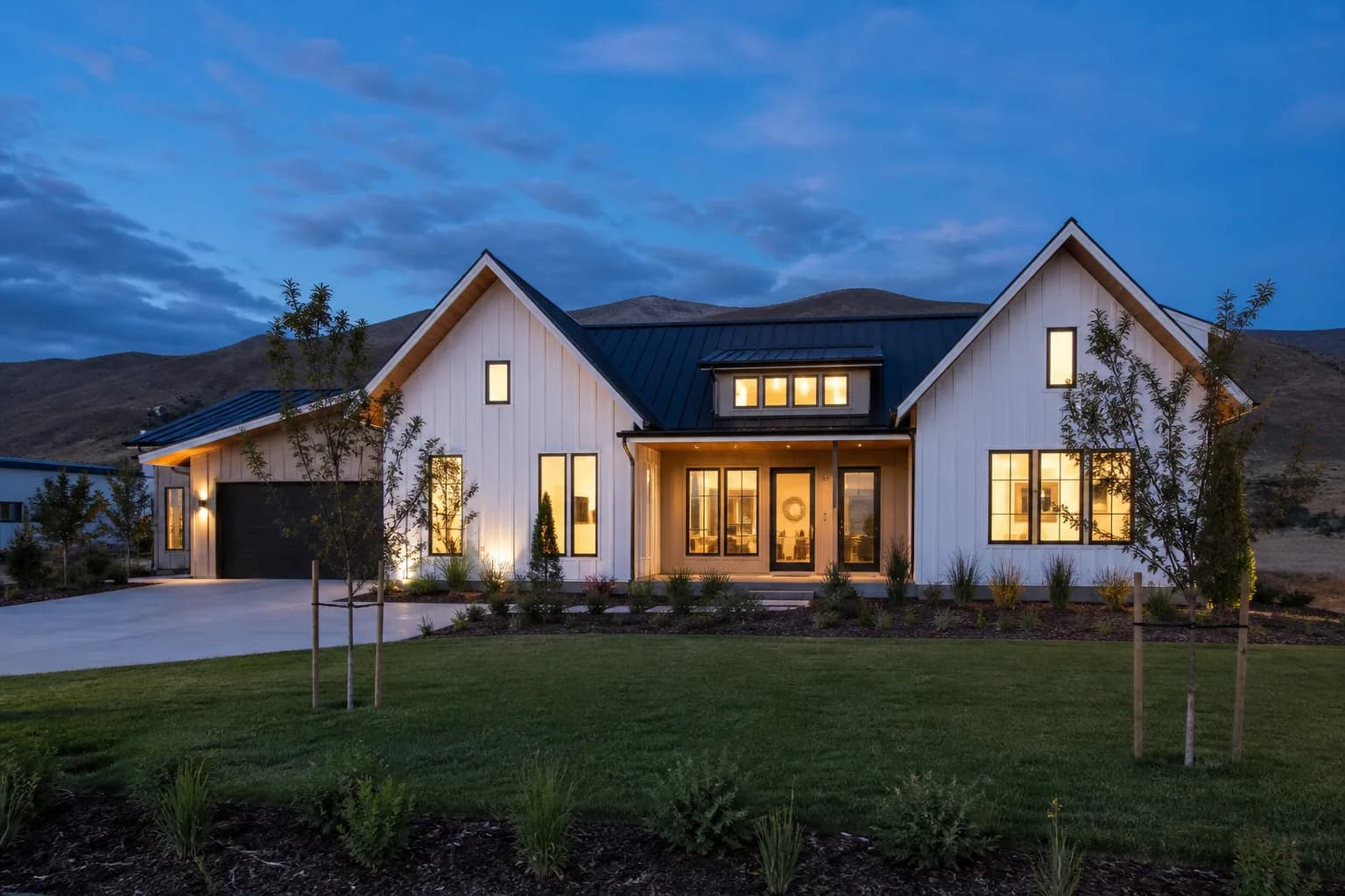 Newly completed modern farmhouse custom home glowing at dusk on a Treasure Valley lot with the Boise foothills behind